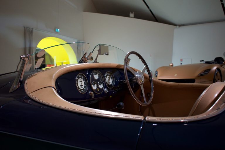 Interior of a vintage car showing a wood-rimmed steering wheel, classic round gauges and tan leather trim