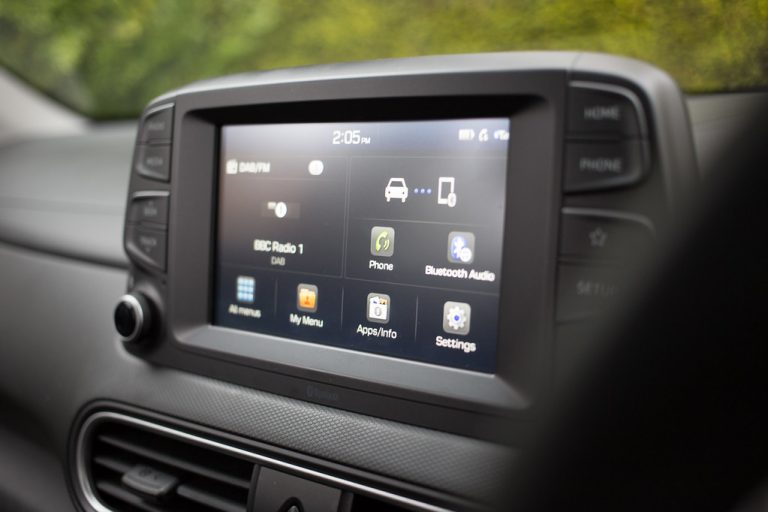 A double-DIN touchscreen infotainment head unit mounted in a car dashboard, showing radio and media controls
