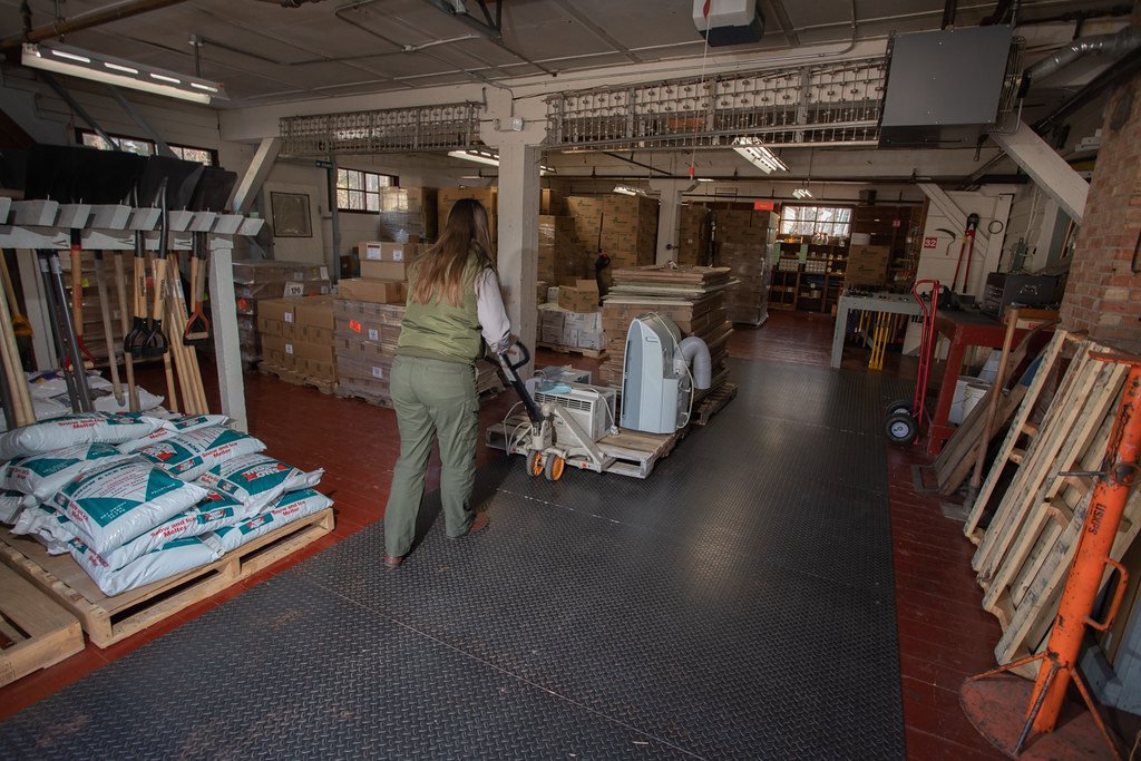 A worker using a manual pallet jack to move a loaded pallet across a concrete warehouse floor