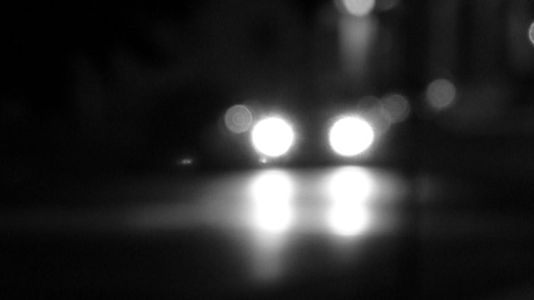 A car's headlights illuminated at night, showing the beam pattern cast onto the road ahead