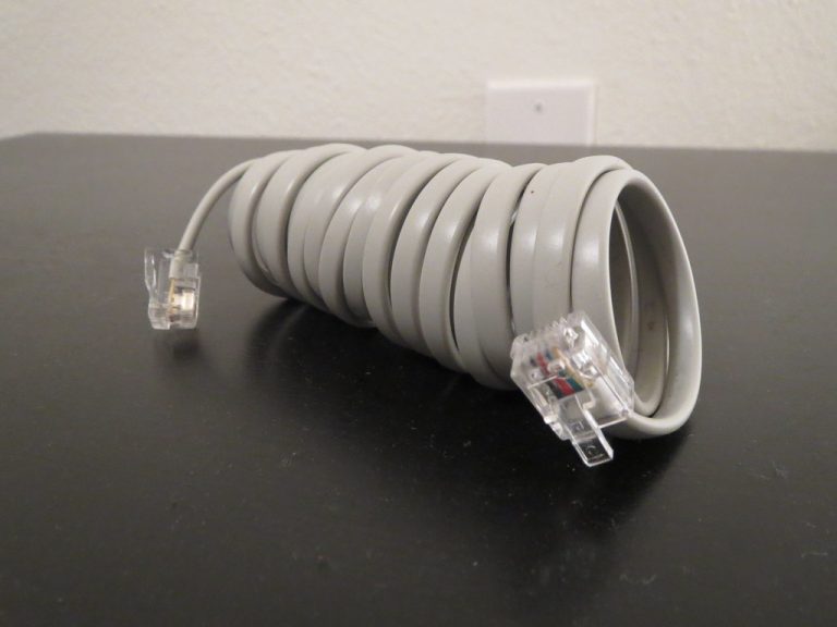 A windshield-mounted radar detector installed inside a car with its coiled power cable running to the dashboard