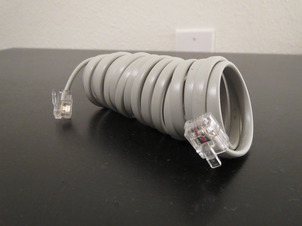 A windshield-mounted radar detector installed inside a car with its coiled power cable running to the dashboard