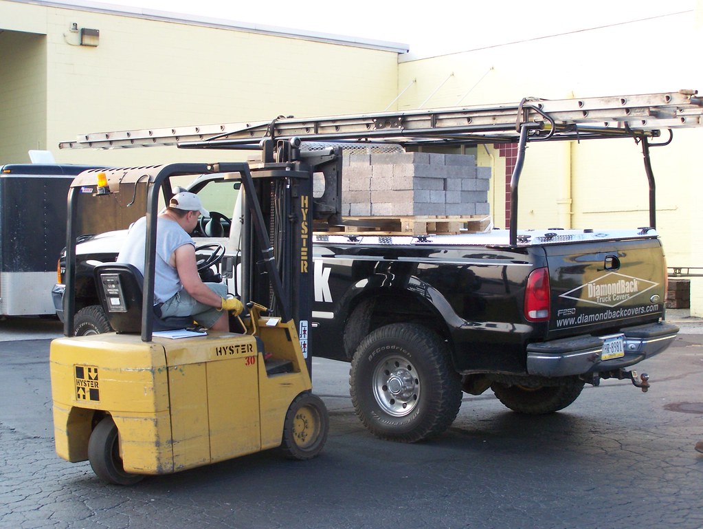 A worker loading a palletized block onto a heavy-duty truck bed cover, illustrating a distributed load on a hard tonneau cover