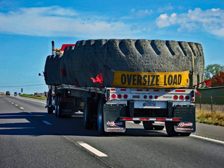 Escort truck displaying an amber warning beacon while accompanying an oversize load.