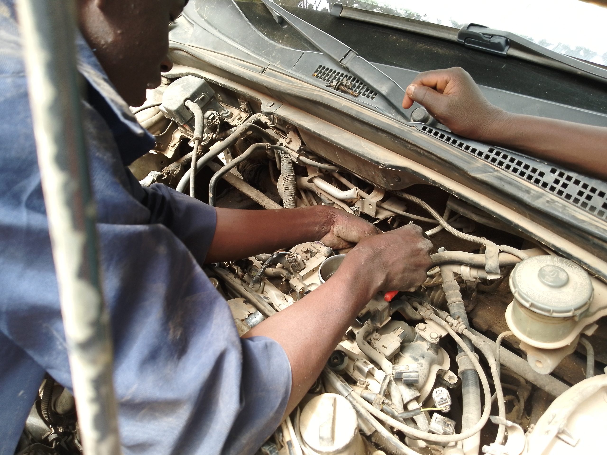 Mechanic reaching into an open engine bay to repair components on a car engine.