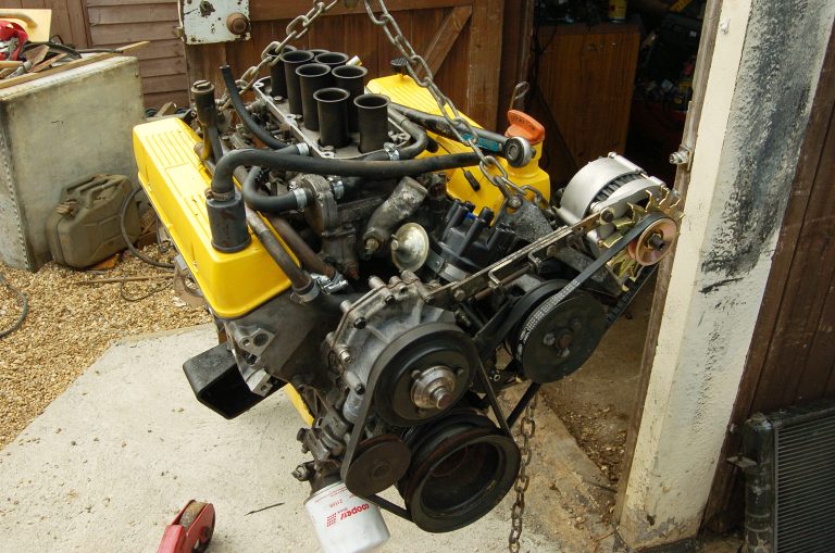 A V8 engine suspended by chains from an engine hoist during a Range Rover restoration.
