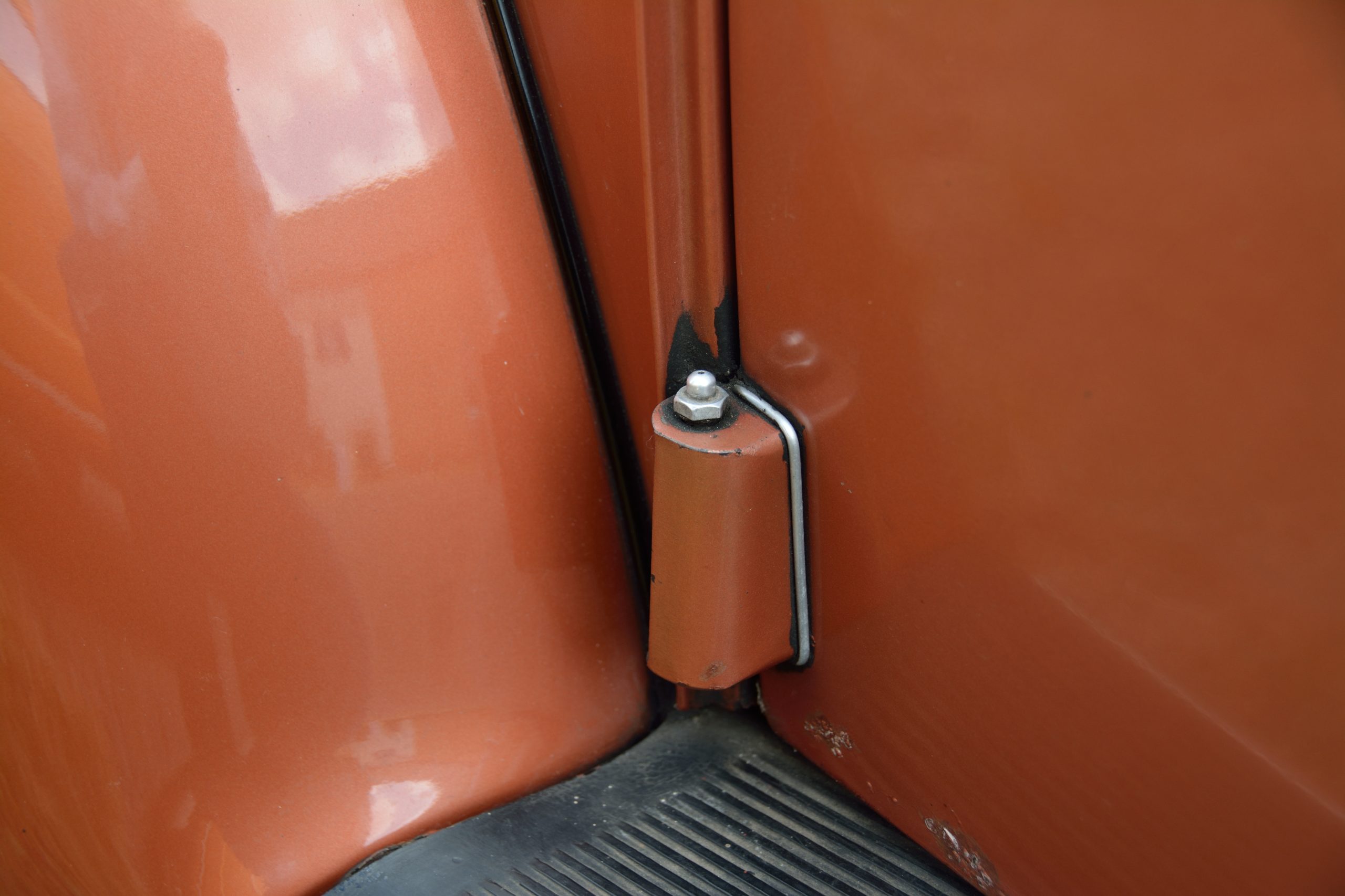 A grease nipple fitting on the door hinge of a classic vehicle, showing a typical automotive lubrication point.