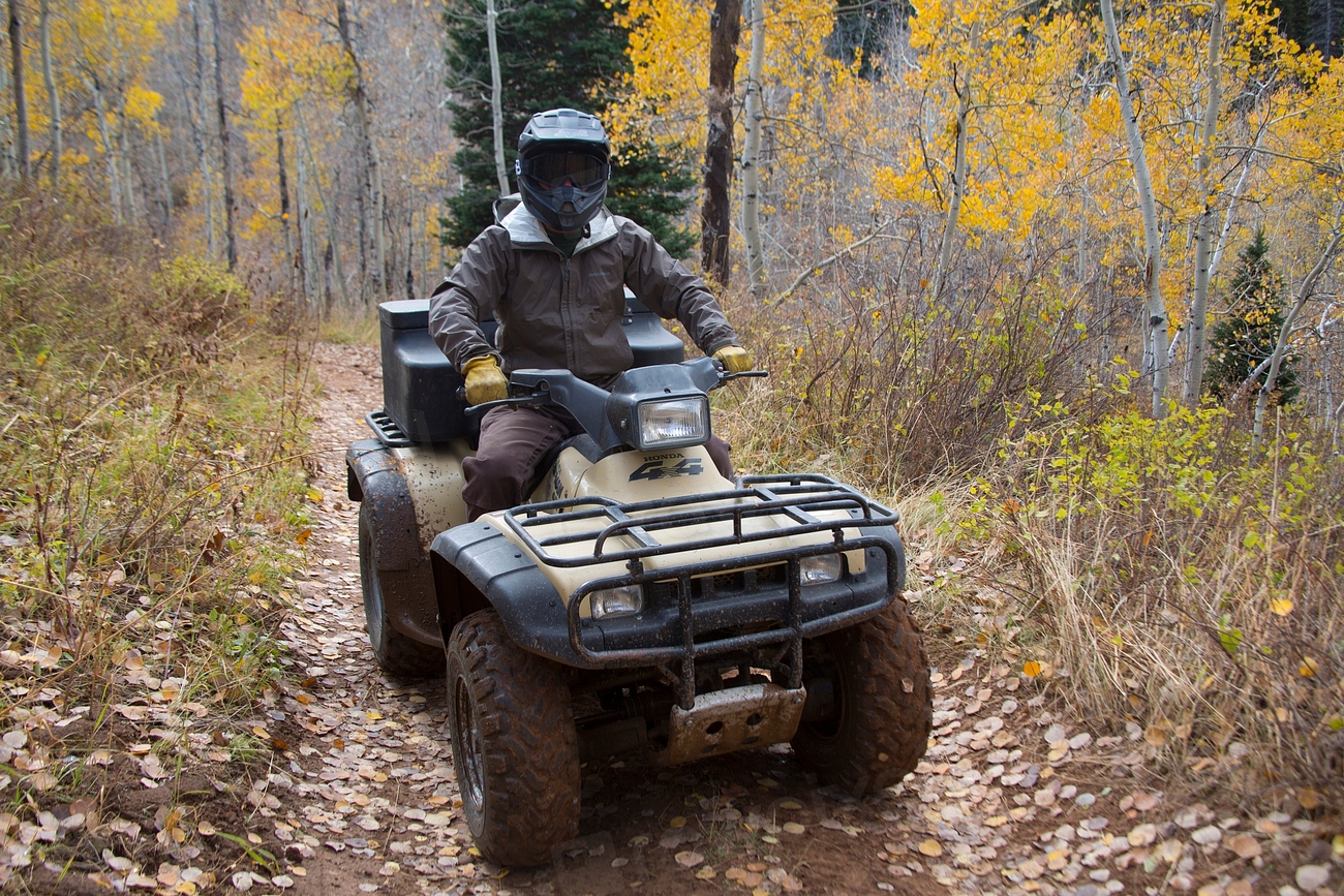 An ATV parked on a dirt trail with a rear cargo rack, the kind of setup a drop basket mounts to for hauling gear.