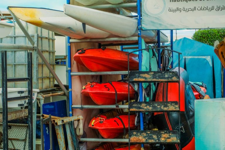 Rows of colorful kayaks neatly stacked on outdoor metal storage racks.