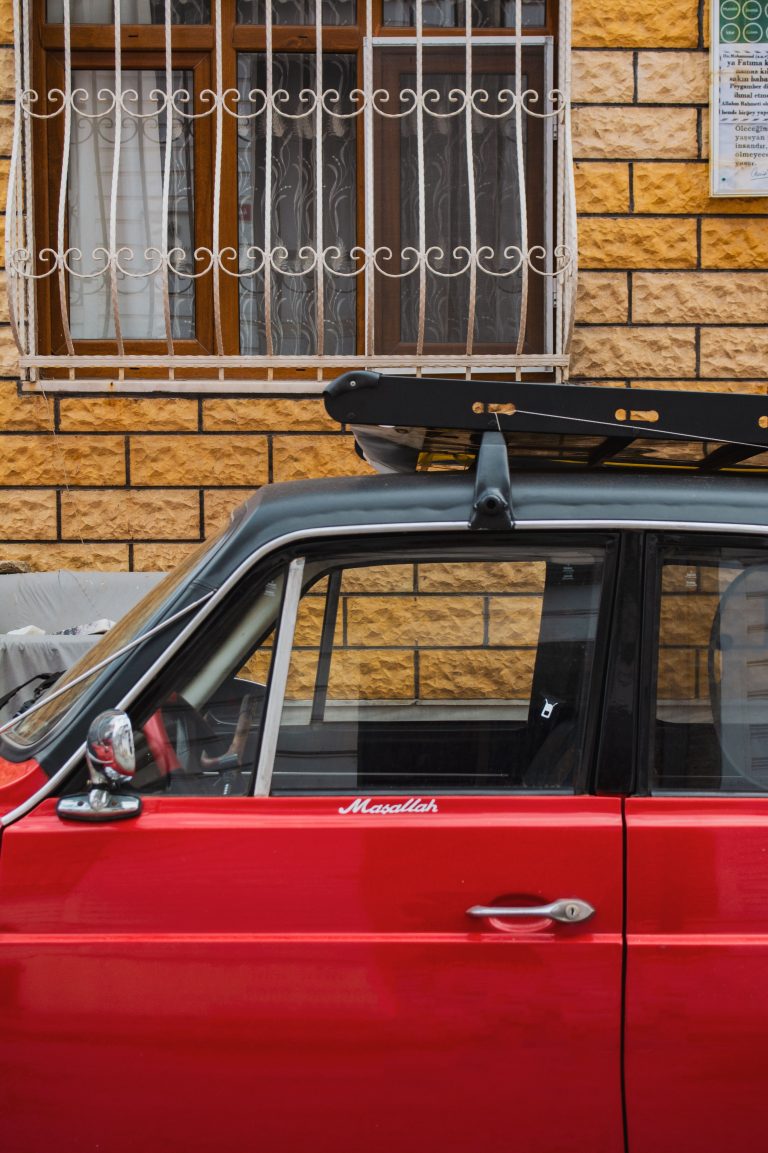 A red car parked outdoors with an empty roof rack mounted on crossbars.