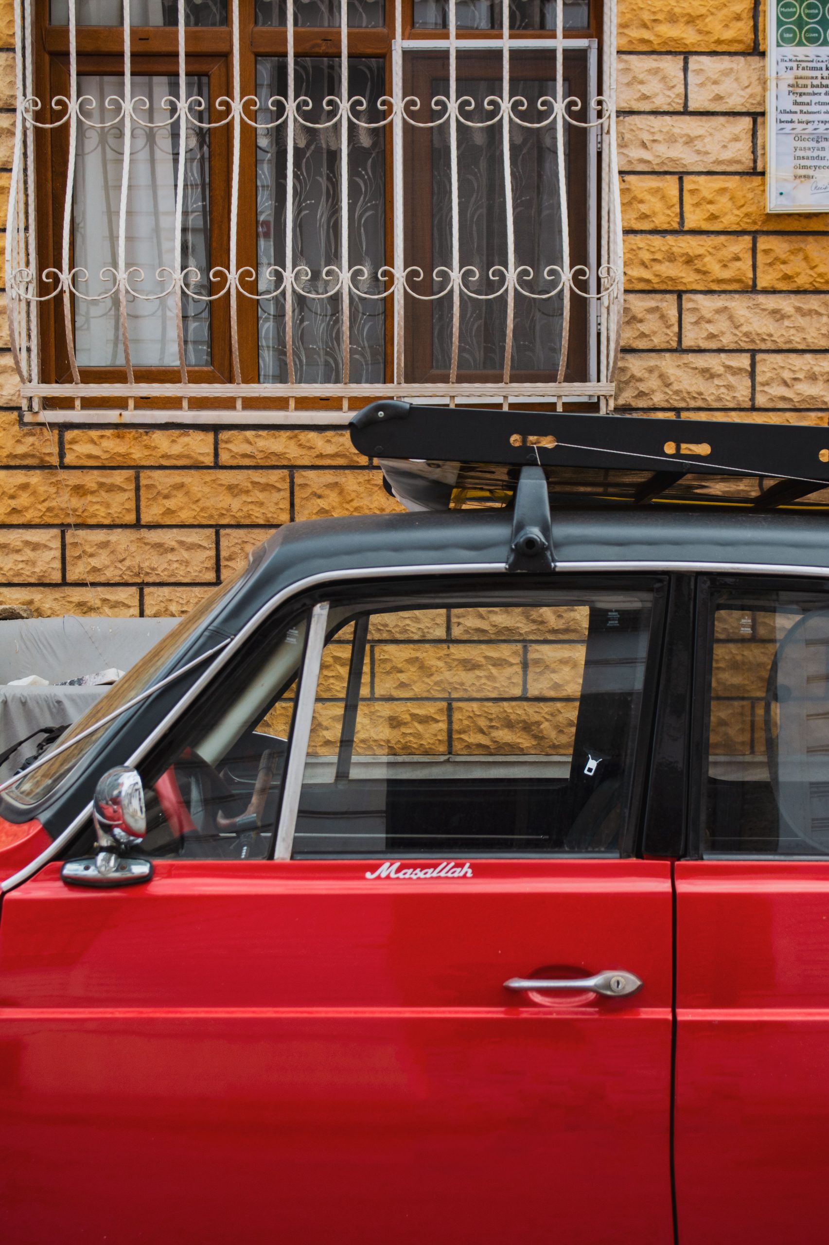 A red car parked outdoors with an empty roof rack mounted on crossbars.