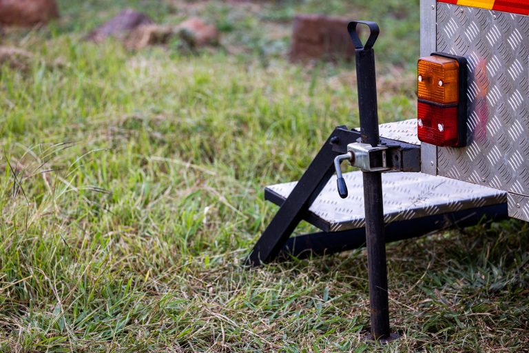 Trailer hitch and tongue jack assembly in a grassy field, showing a coupler ready for locking.